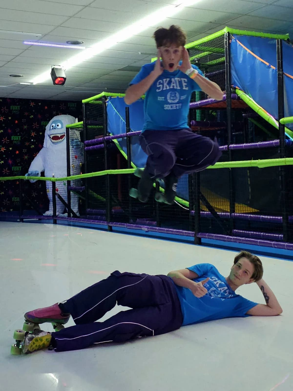 Two Skate Society skaters at a Florida rink — one mid-jump over an obstacle course, one striking a pose on the floor in matching crew tees.